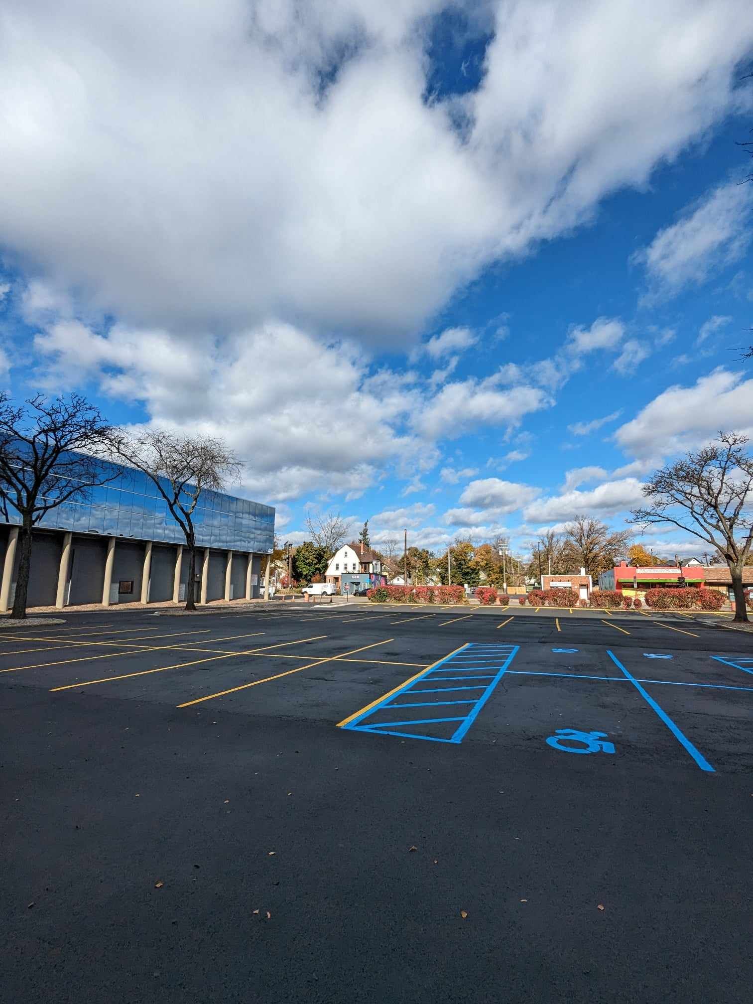 Empty parking lot with blue handicap spaces, blue building, and a partly cloudy sky.