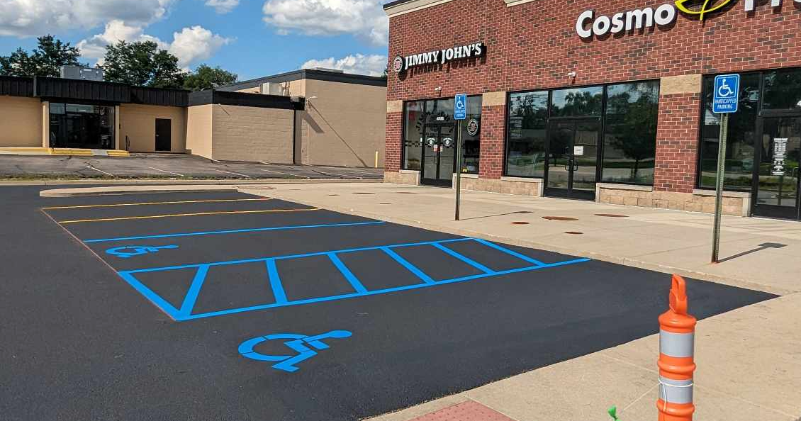 Parking lot with blue handicap parking spaces in front of a brick building; an orange traffic cone is in the foreground.