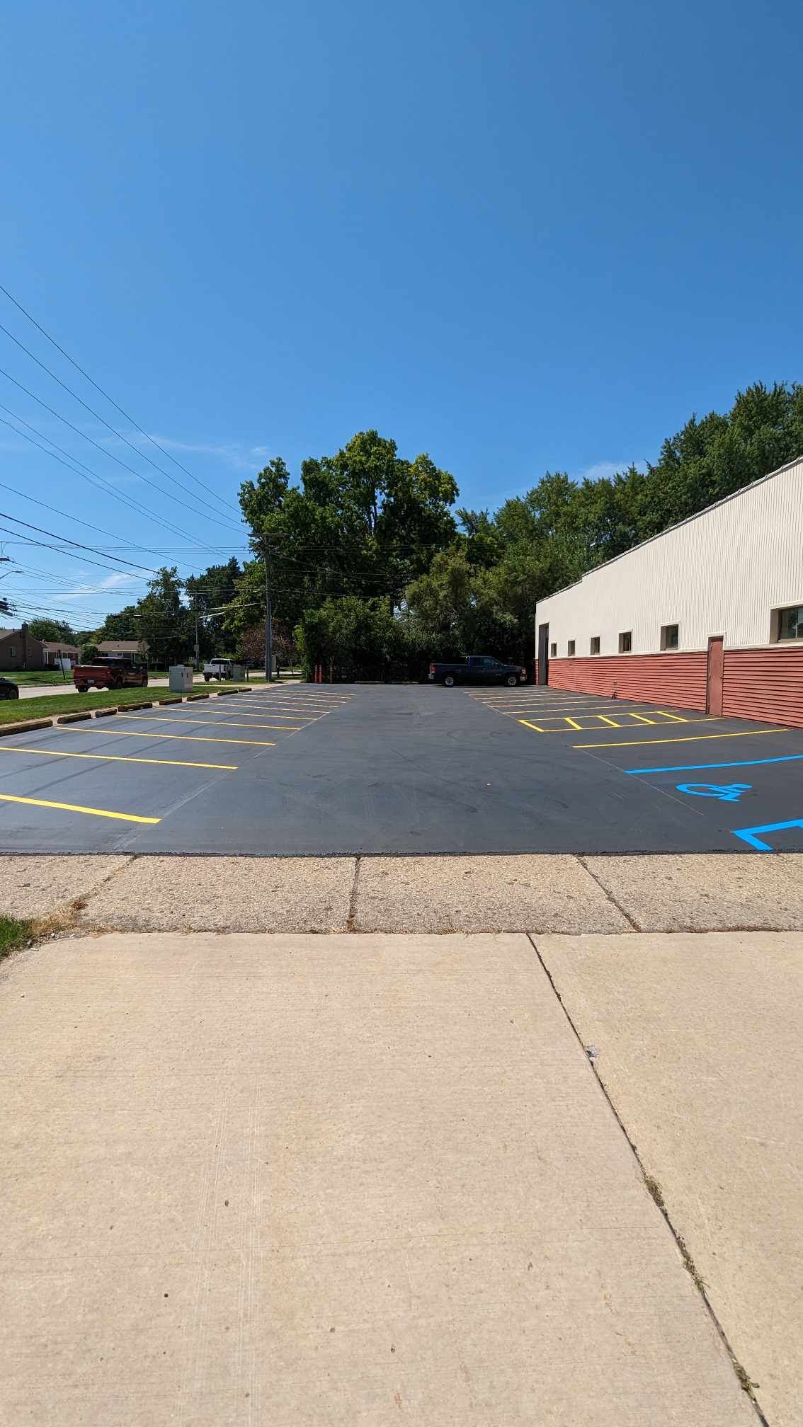 Paved parking lot with painted spaces, building on the right, trees and blue sky.