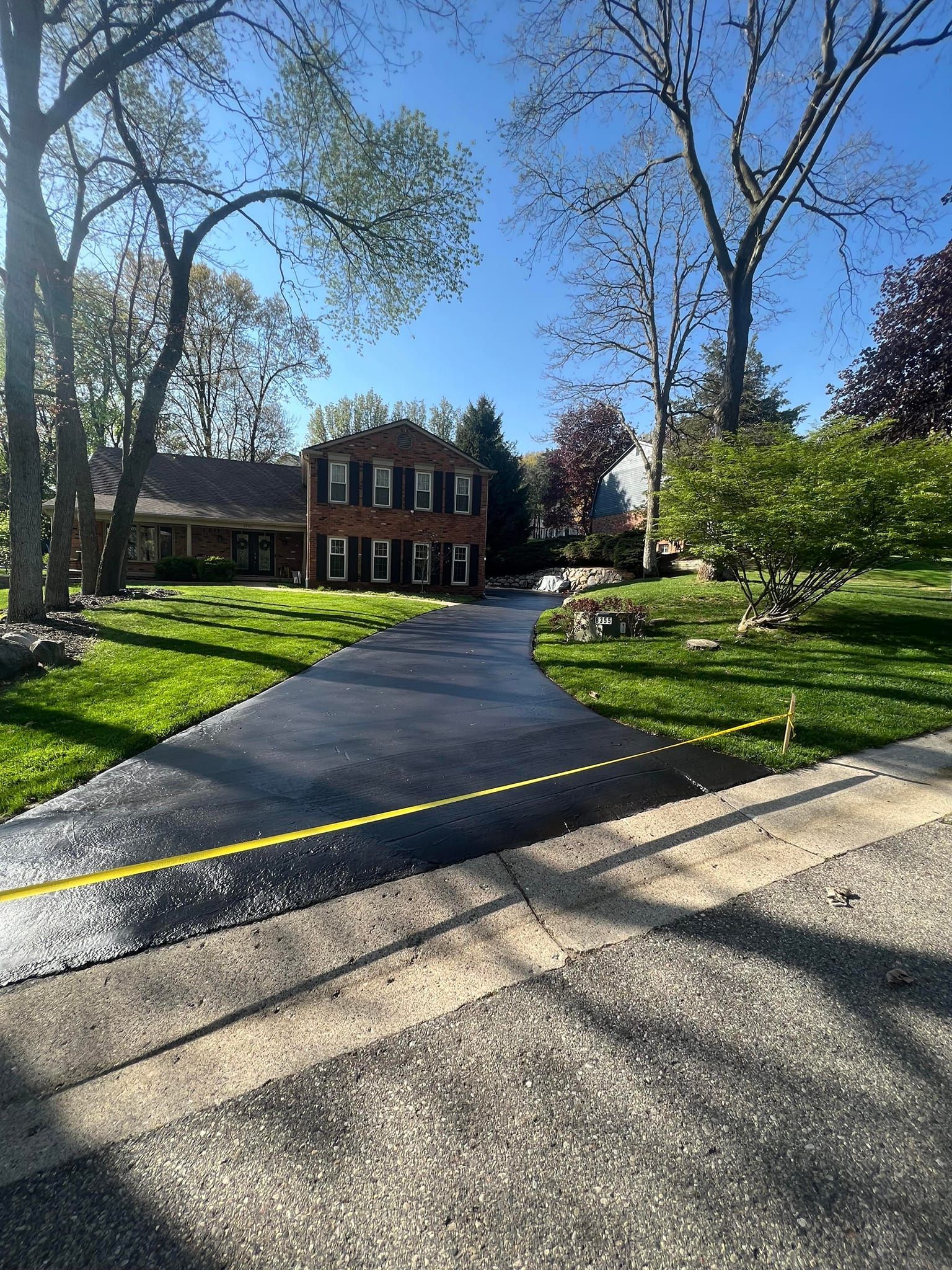 Two-story brick house with newly paved driveway; green lawn and trees under a clear sky.