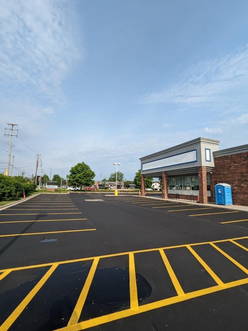 Empty parking lot with yellow lines, a small building with a canopy, and a blue portable toilet on a sunny day.