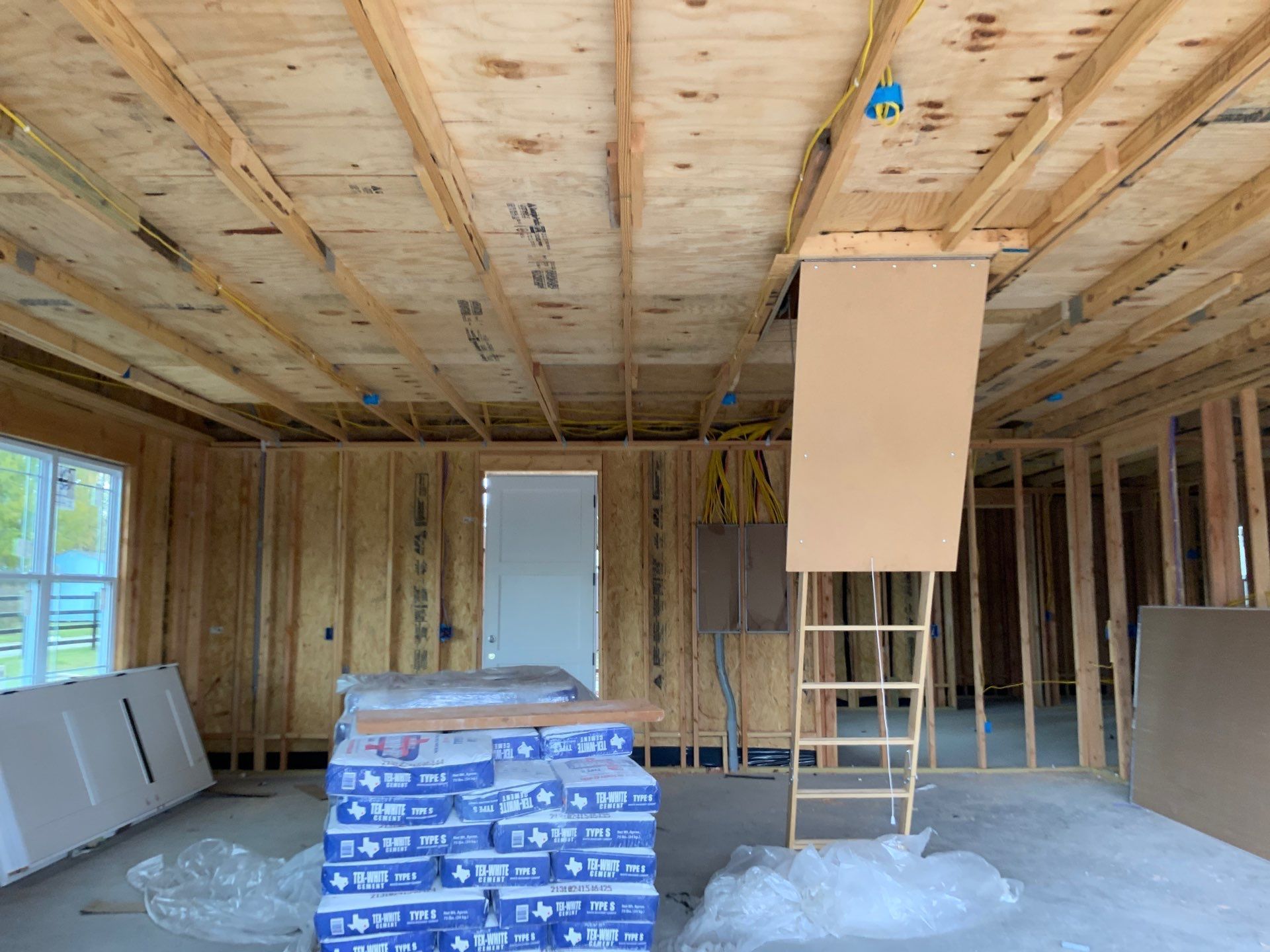 A room in a house under construction with wooden beams and a ladder.