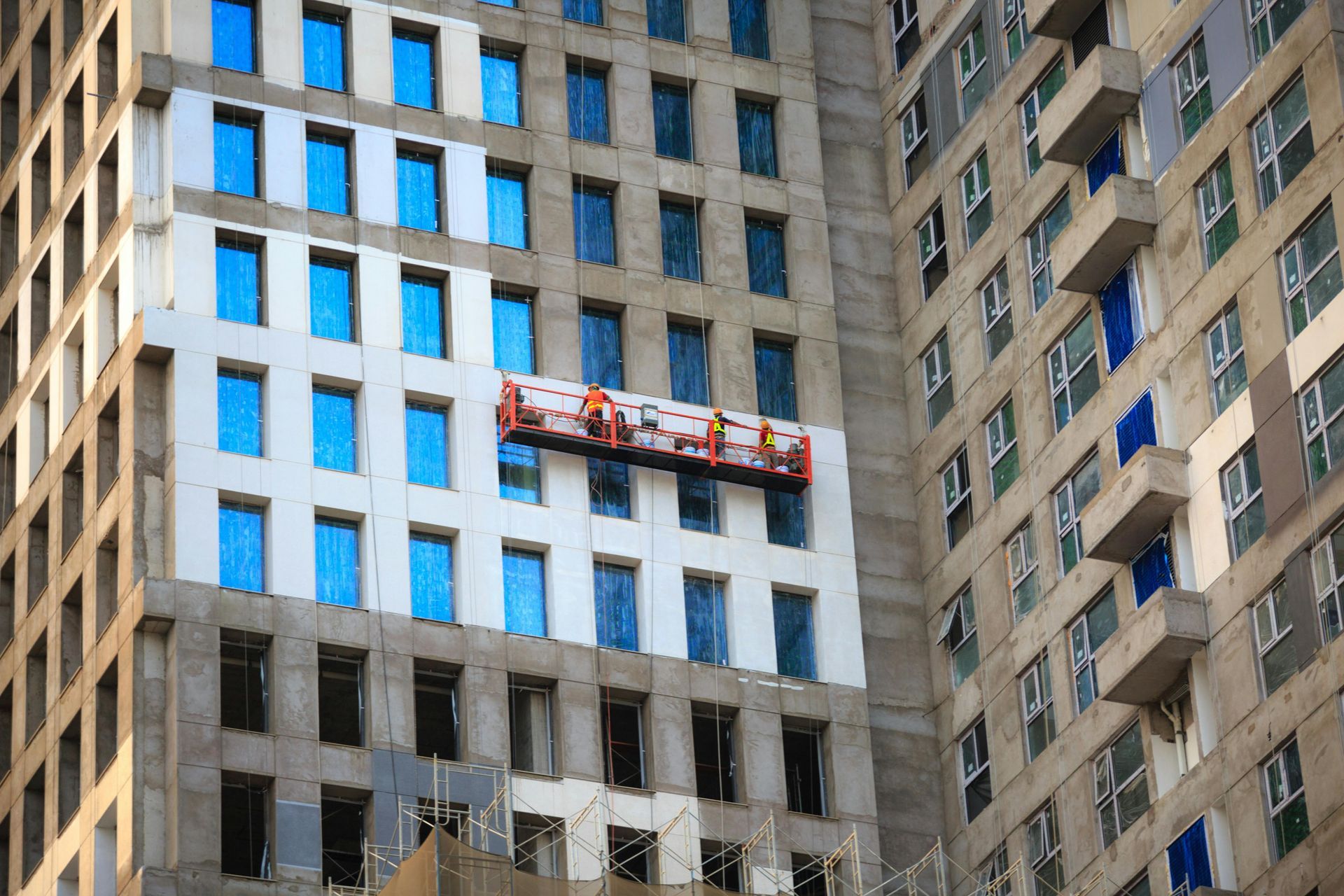 Building under construction with workers on a suspended platform.
