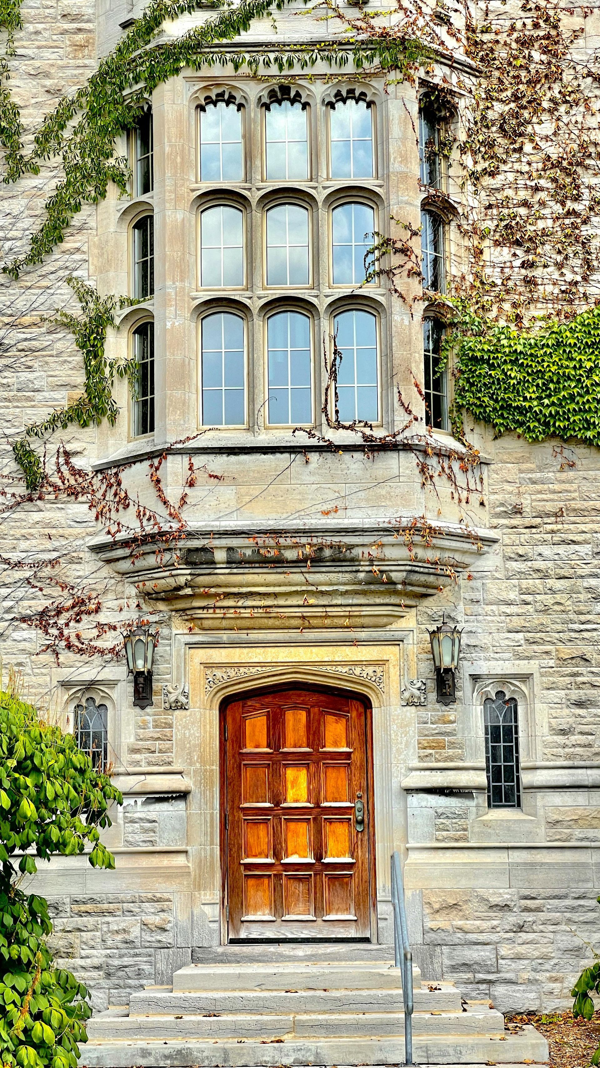 Stone building with ornate wooden door and multi-paned windows, covered in ivy.