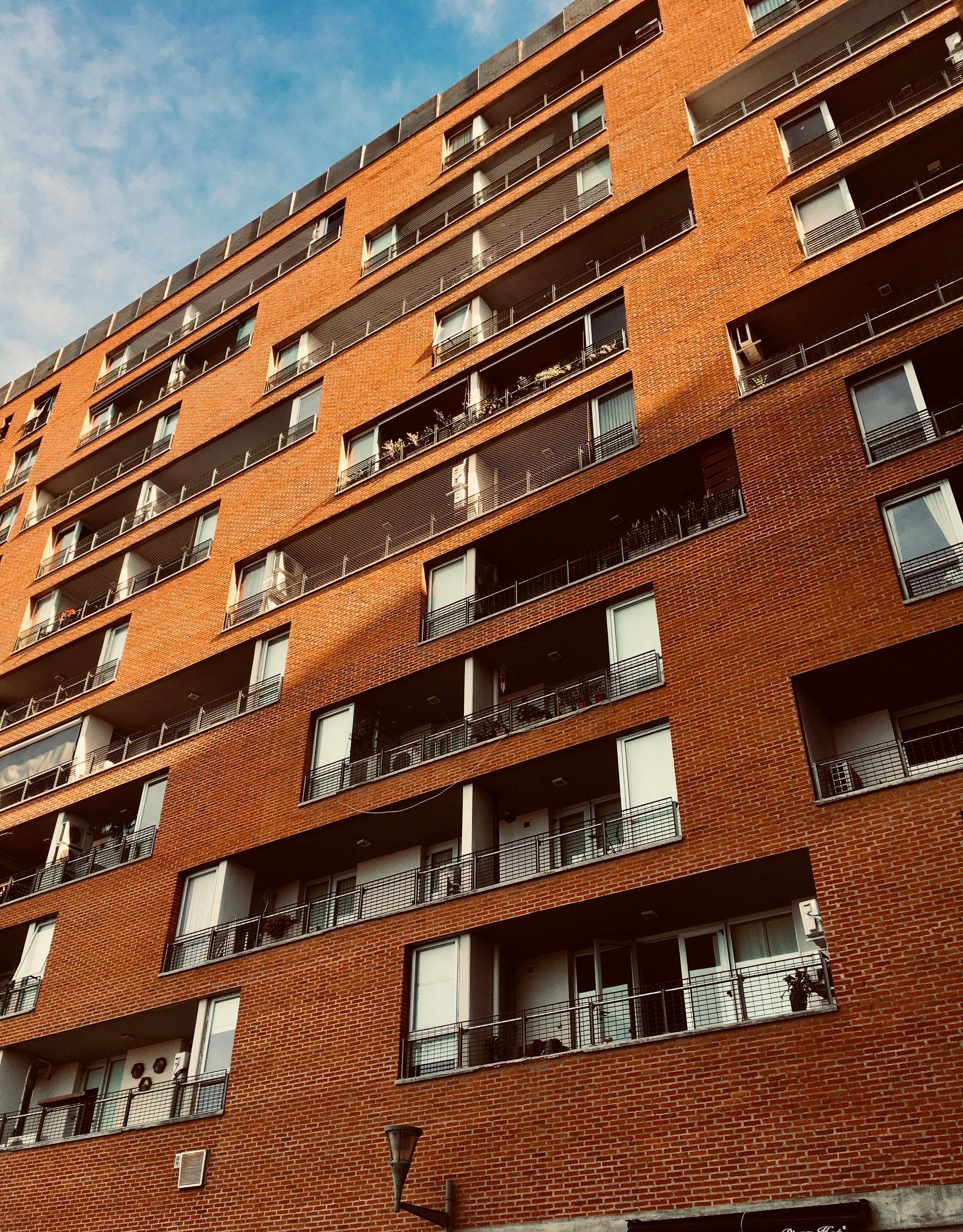 Red brick apartment building against a blue sky; balconies on each level.