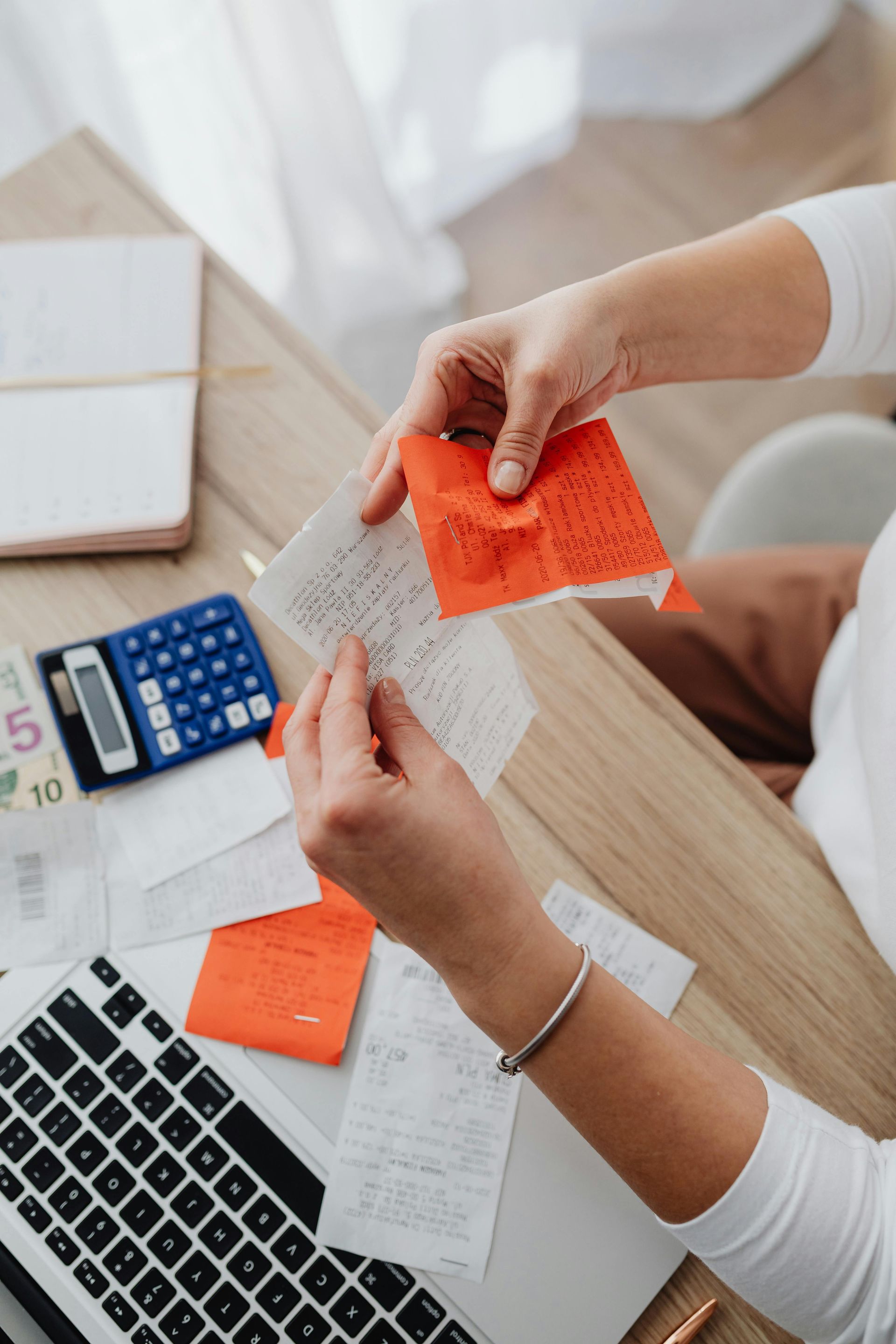 Hands sorting receipts with a calculator and laptop on a desk, possibly for budgeting.