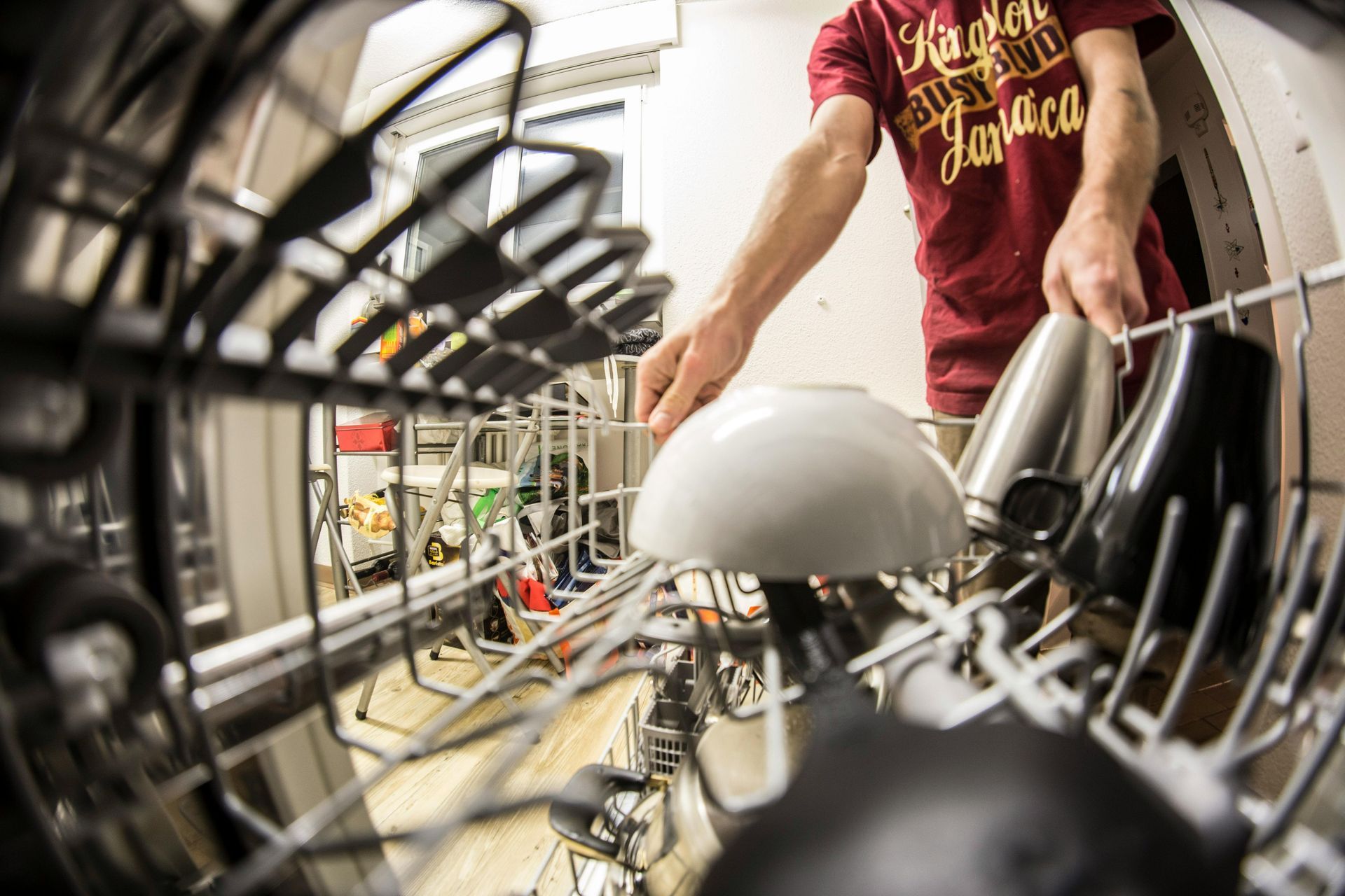 A picture from the inside of a dishwasher pointing out, and looking at a man who is putting a bowl into the dishwasher.