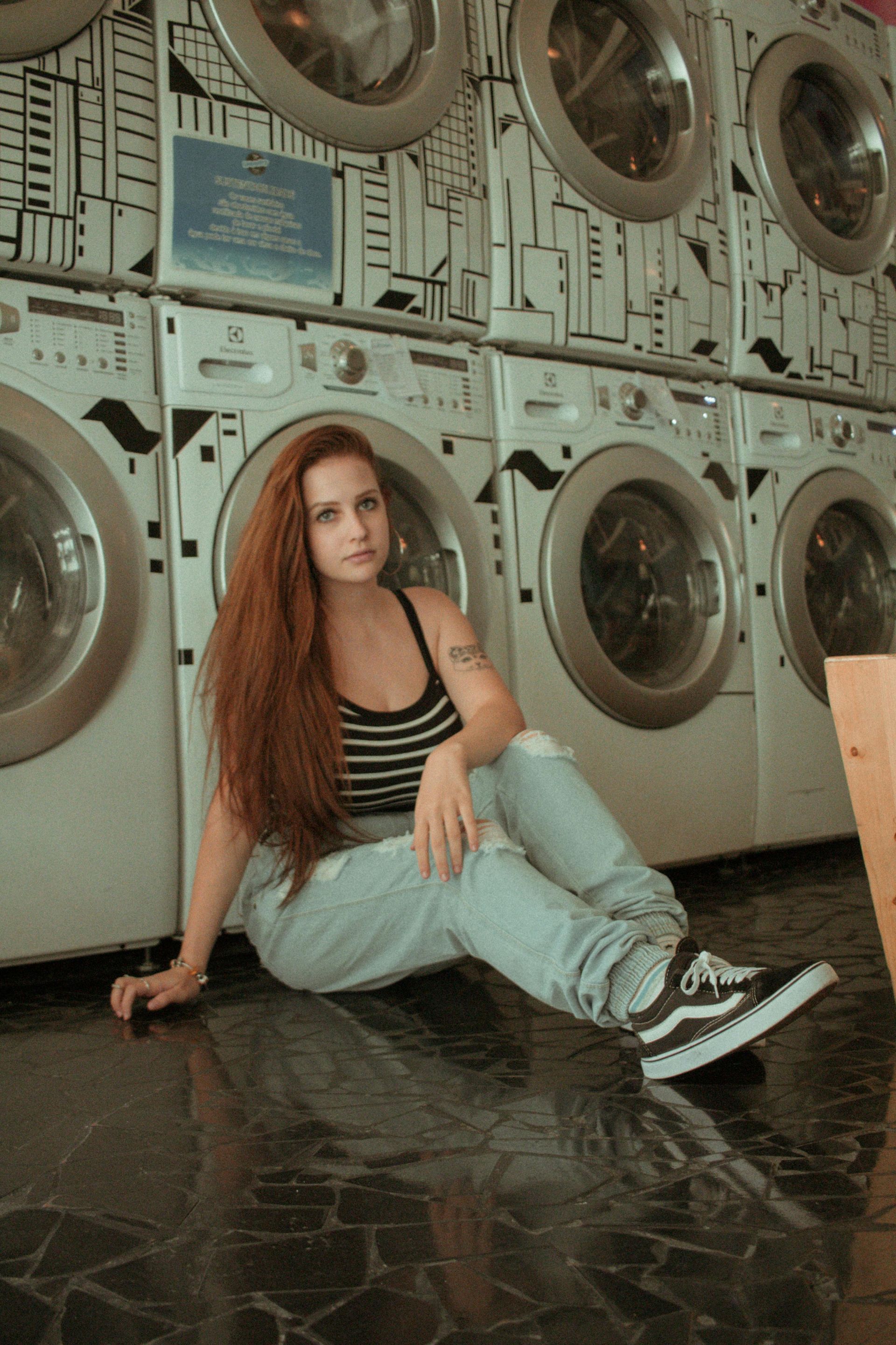 A woman in front of multiple washing machines, sitting down and looking at the camera.