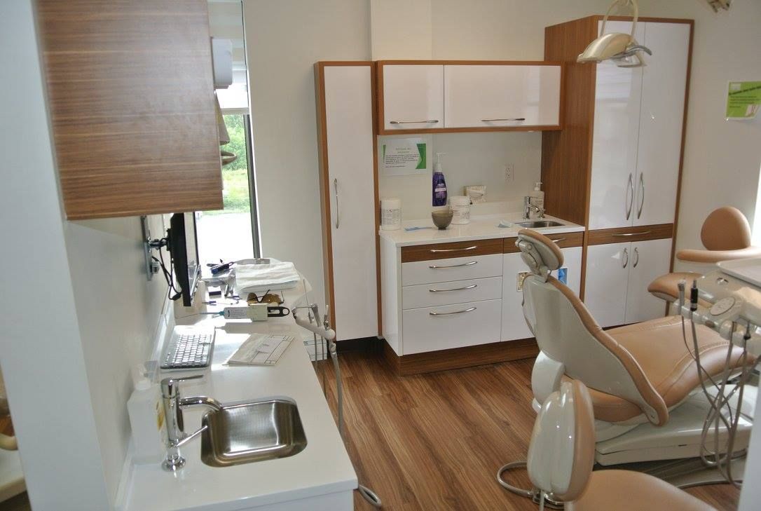 Un cabinet dentaire avec une chaise dentaire, un lavabo et des armoires.