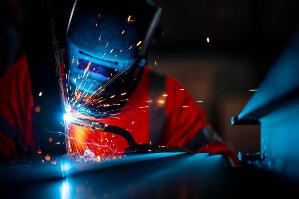 A man wearing a welding helmet is welding a piece of metal.
