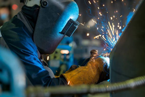 A man is welding a piece of metal in a factory.
