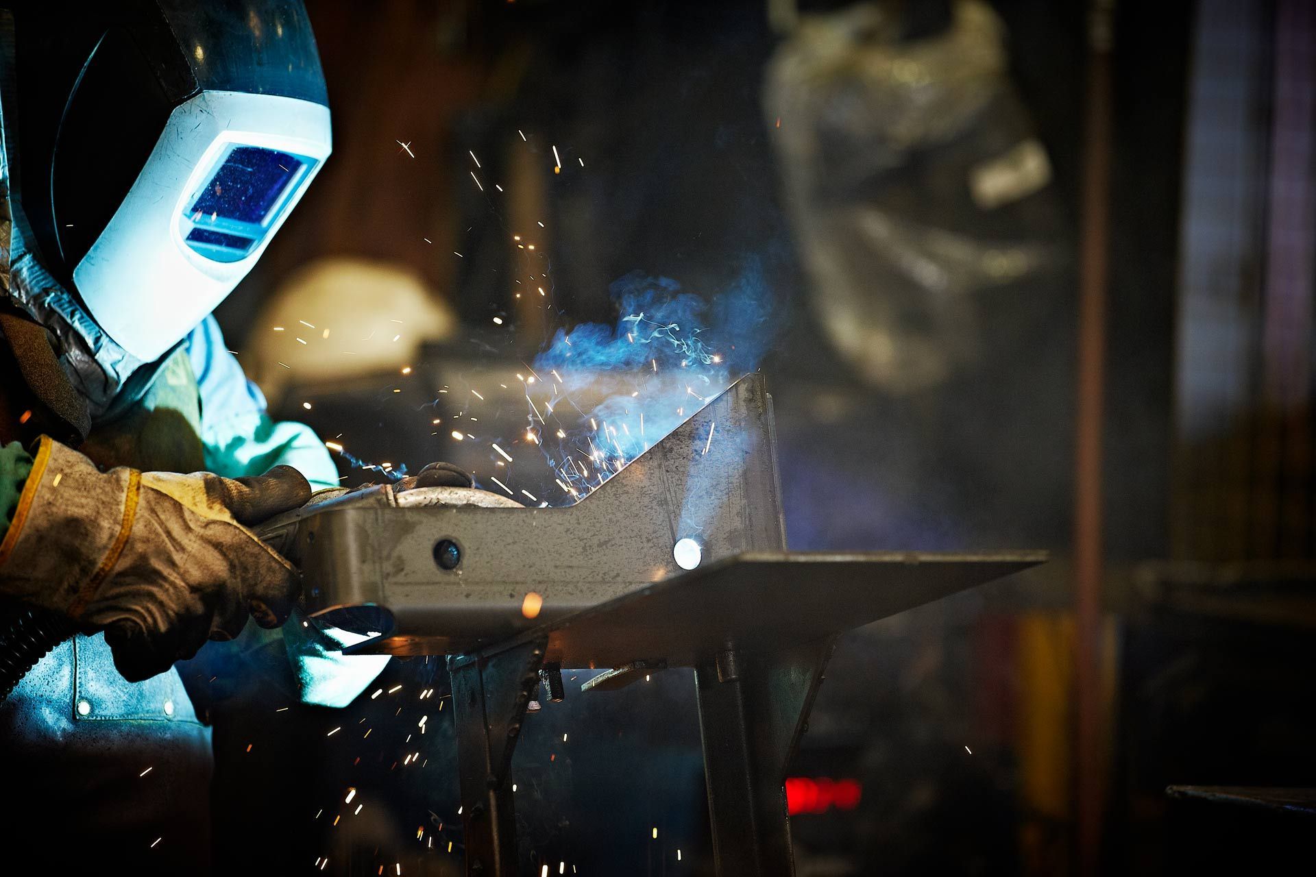 A man wearing a welding mask is welding a piece of metal.