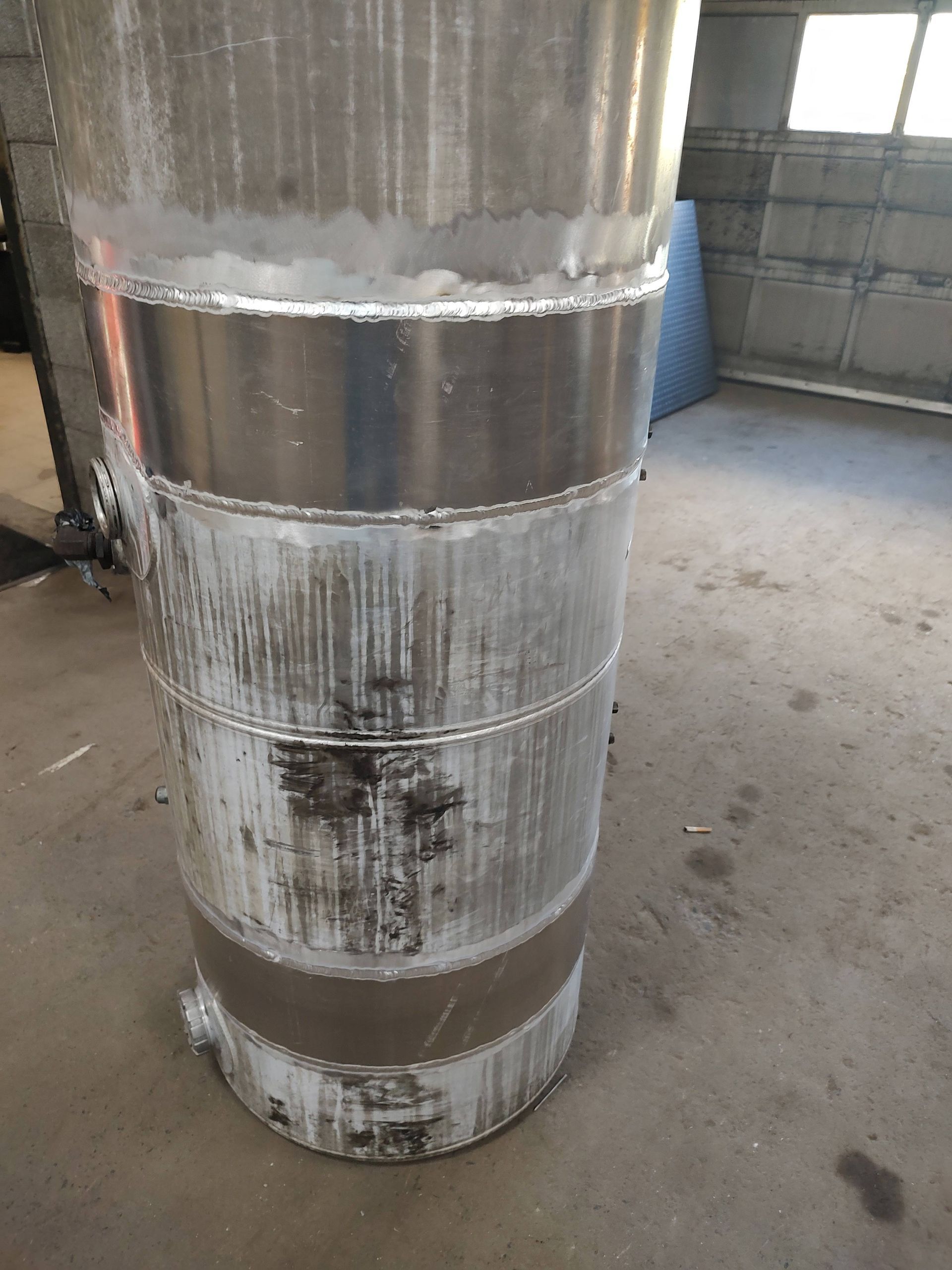 A large metal barrel is sitting on the floor in a garage.