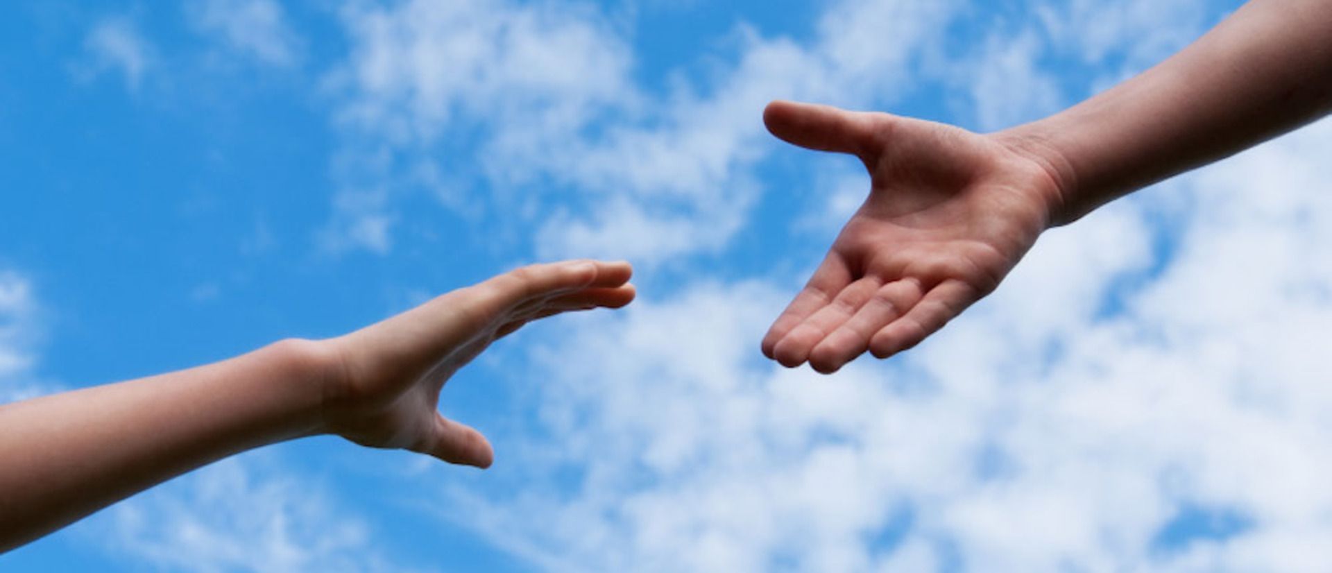 Two hands reaching out towards each other with a blue sky in the background