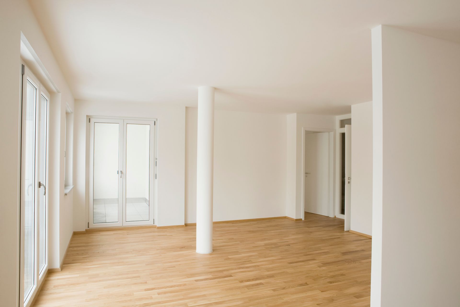 An empty living room with hardwood floors and white walls.