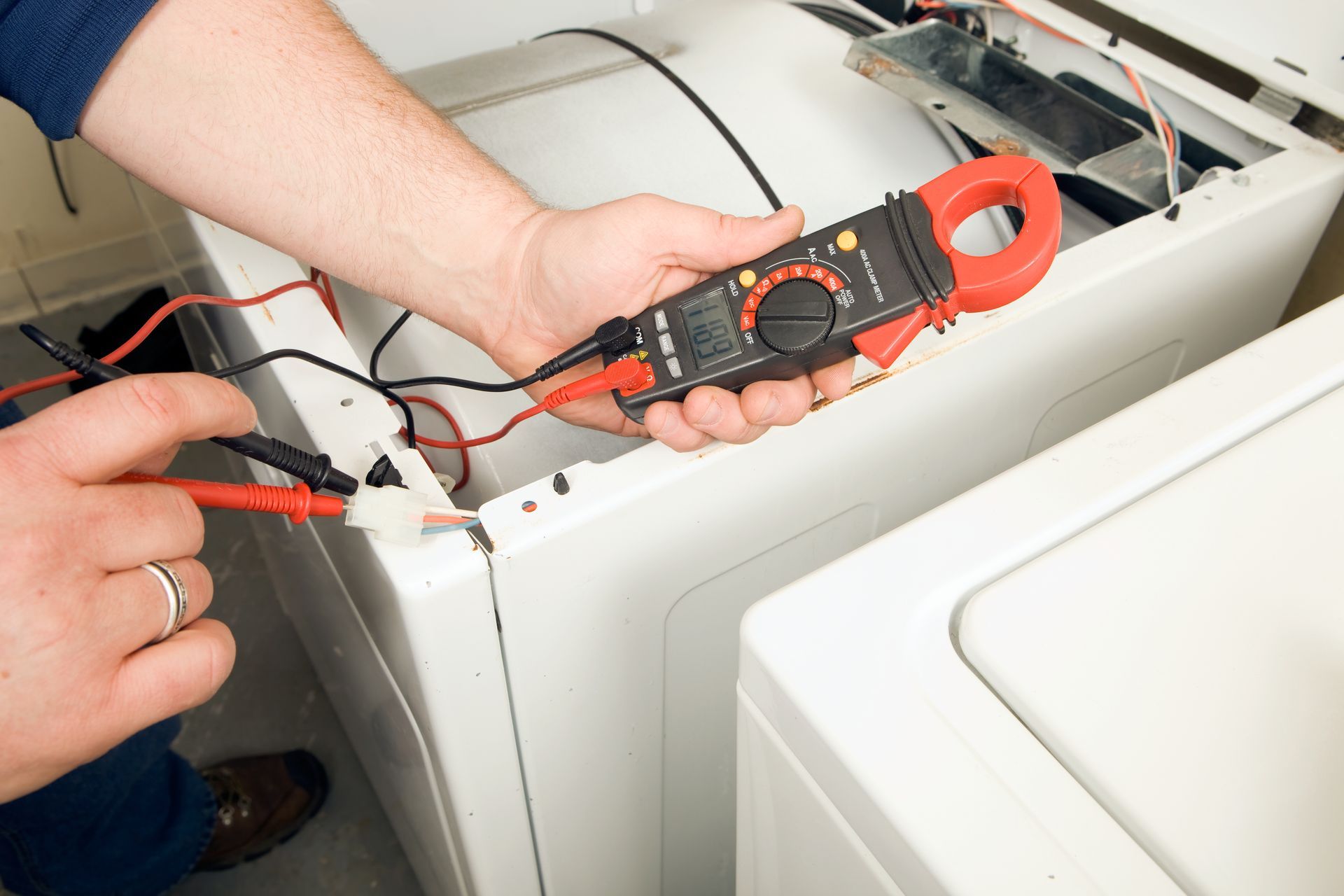 A man is working on a washing machine with a clamp meter.