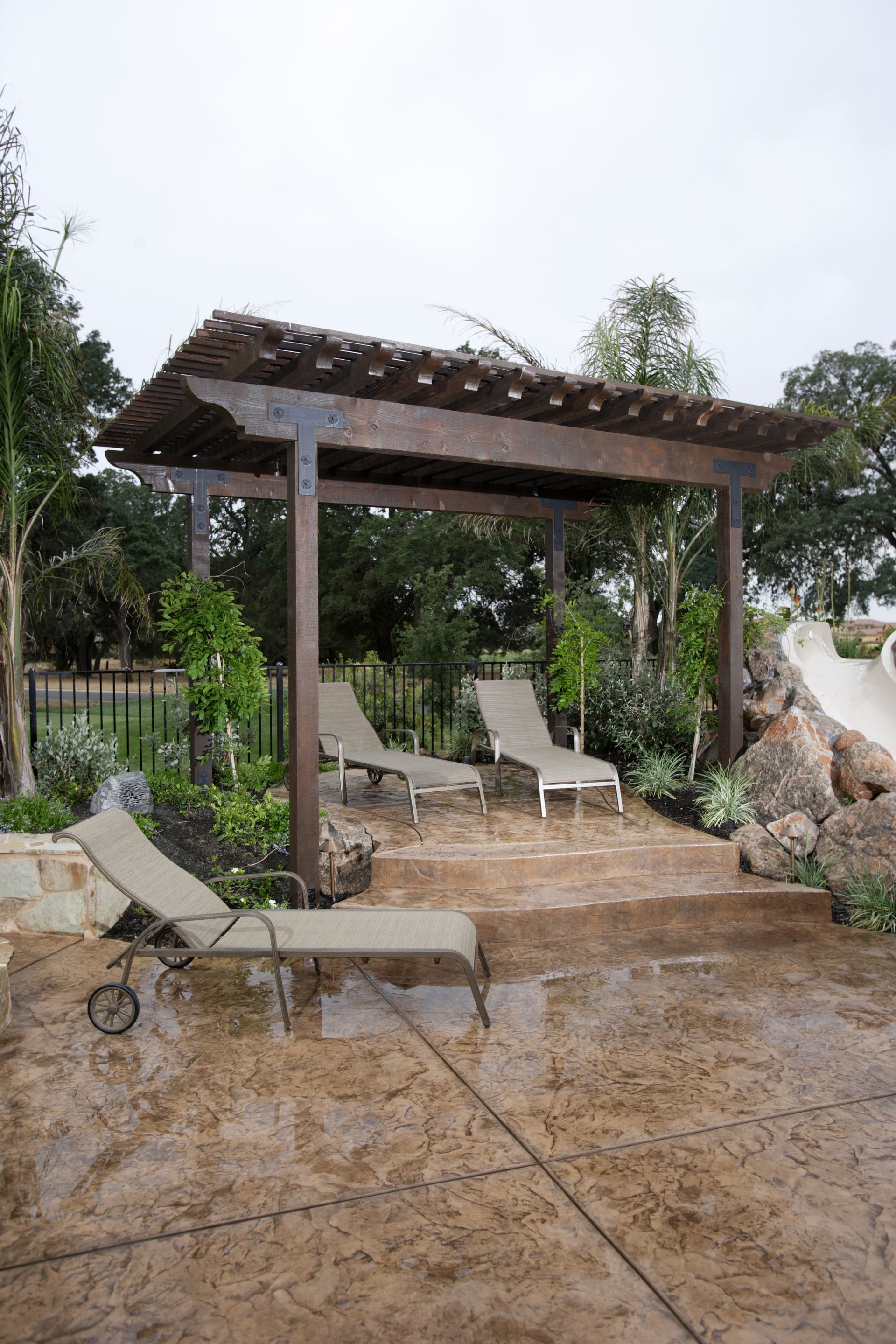 A patio with chairs and a pergola on a rainy day.