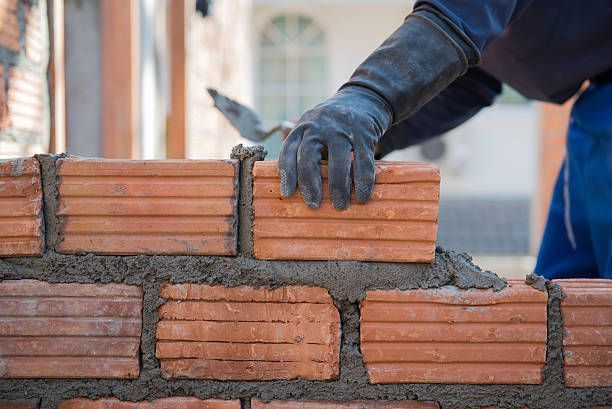A man is laying bricks on top of a brick wall.