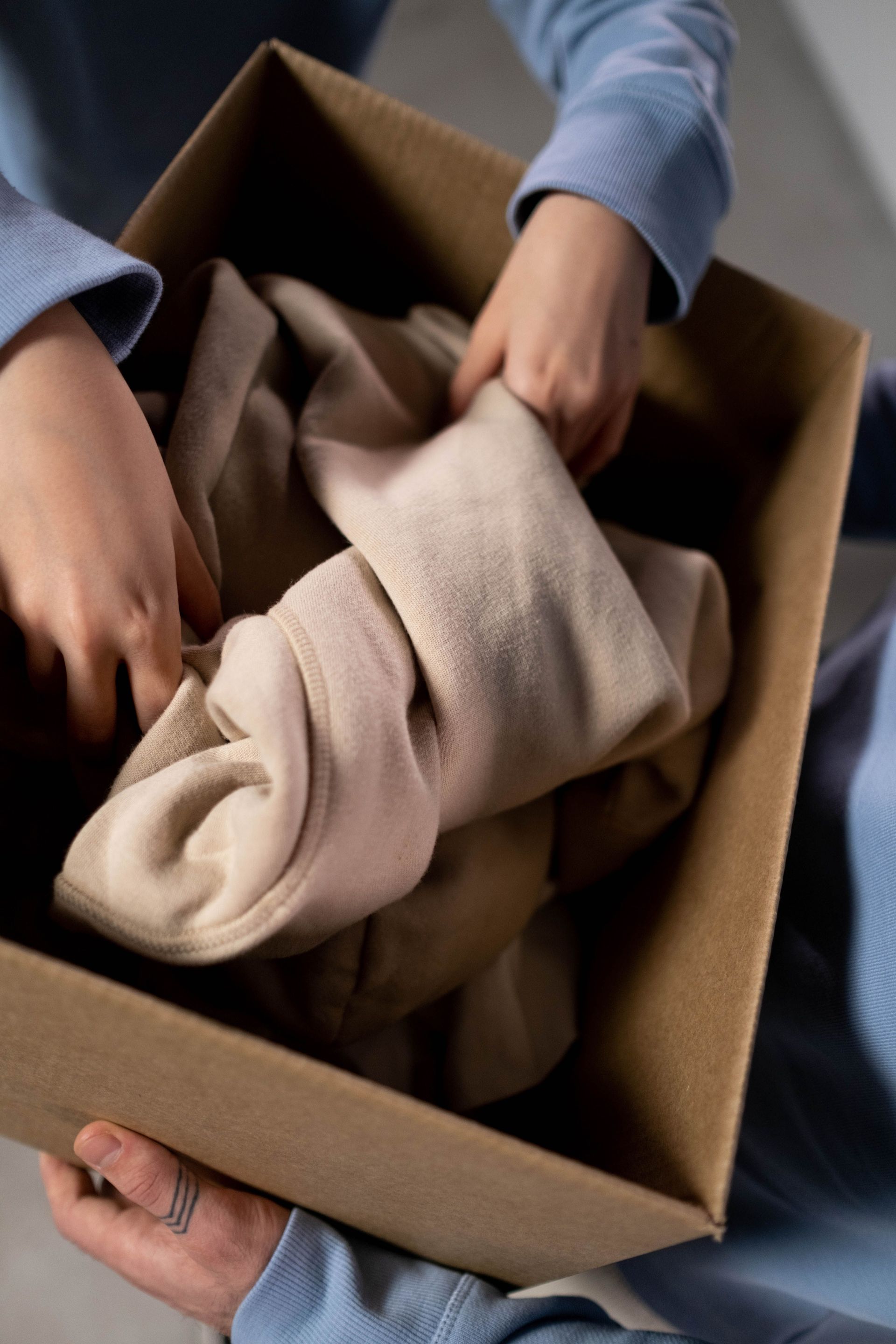 Hands unpack a beige blanket from a cardboard box.