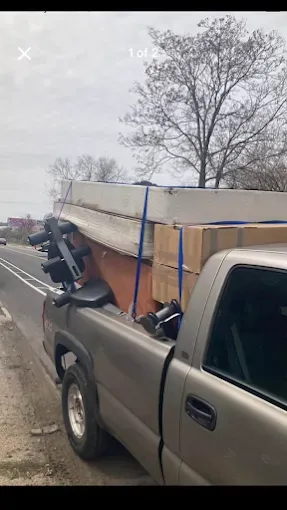 Pickup truck hauling a large plywood load secured with blue straps on a roadside