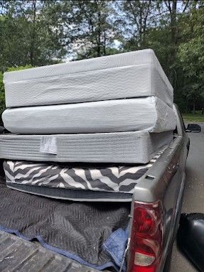 Mattresses stacked in the bed of a pickup truck outdoors, with trees in the background.