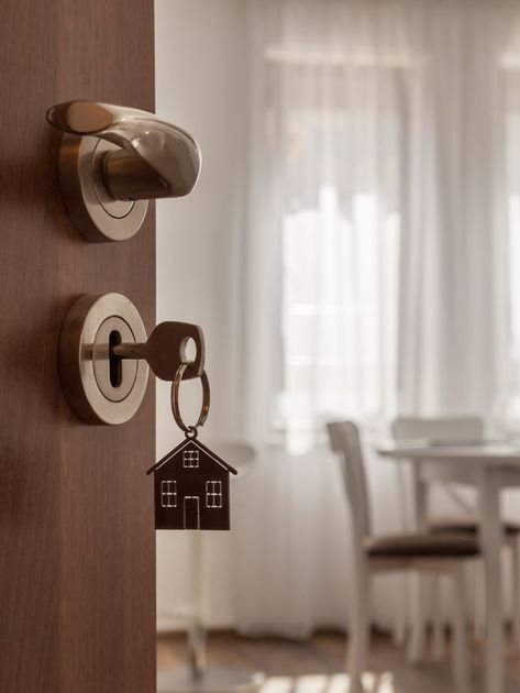 Front door lock with key and house keychain, opening to a bright room with sheer curtains and a table