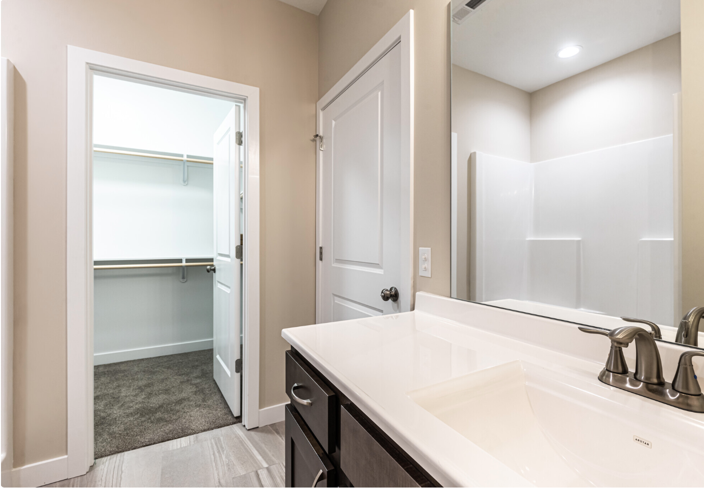 Bright bathroom with vanity and mirror beside an open walk-in closet with white shelving and gray carpet.