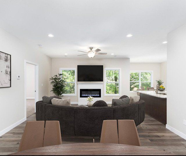 Bright open living room with dark sectional, fireplace TV, ceiling fan, and wood floors