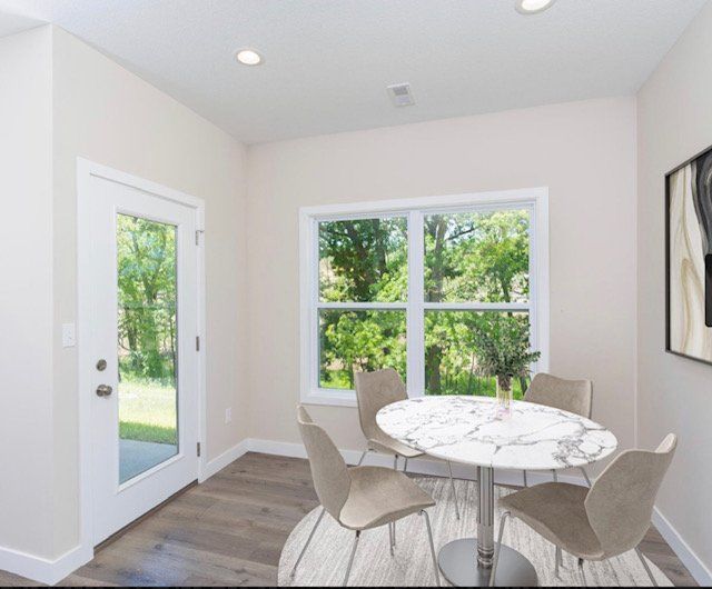 Bright dining nook with a round table, four chairs, white walls, and large windows overlooking greenery.