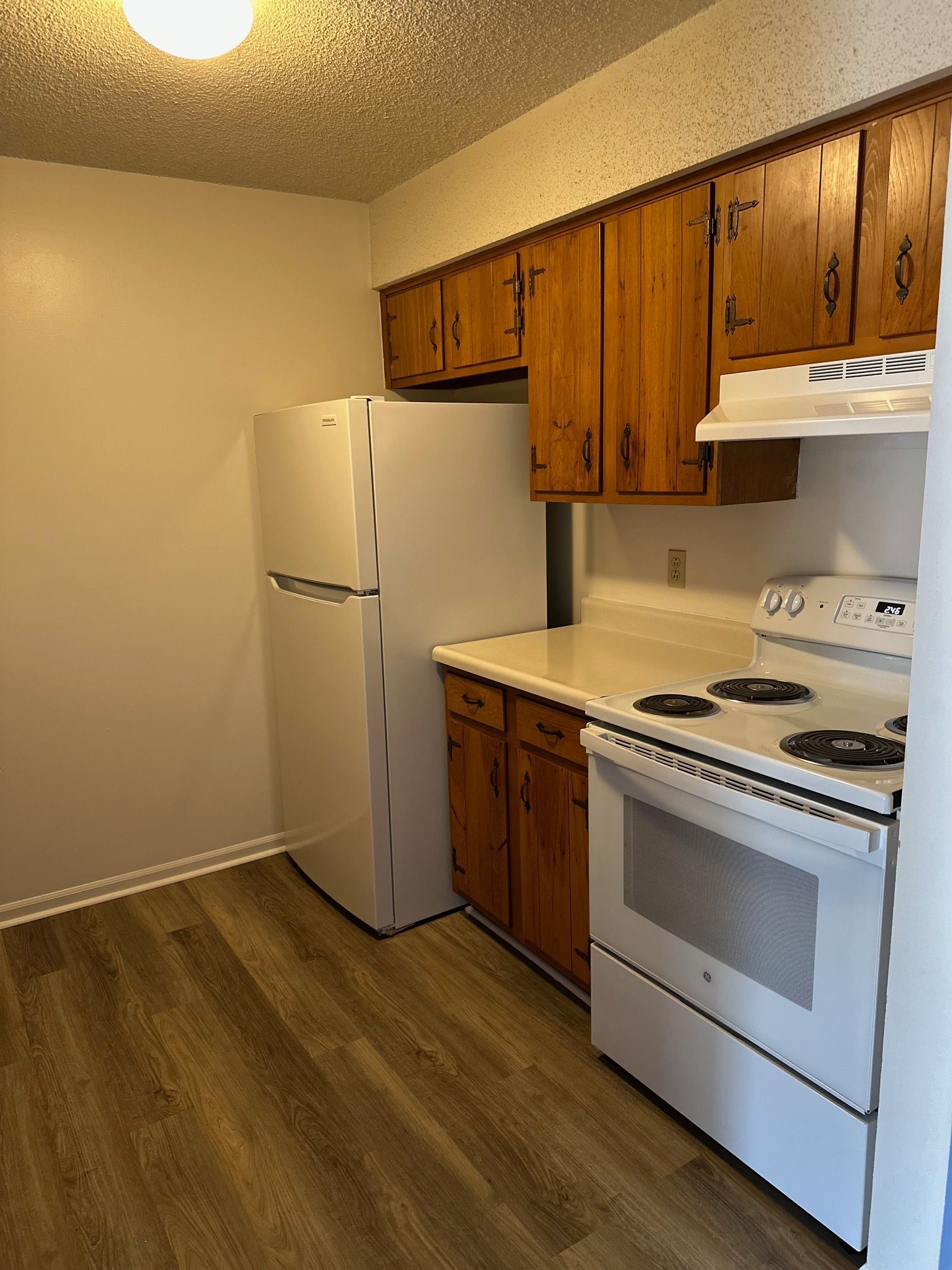 Small kitchen with white appliances, wood cabinets, and wood-look flooring.