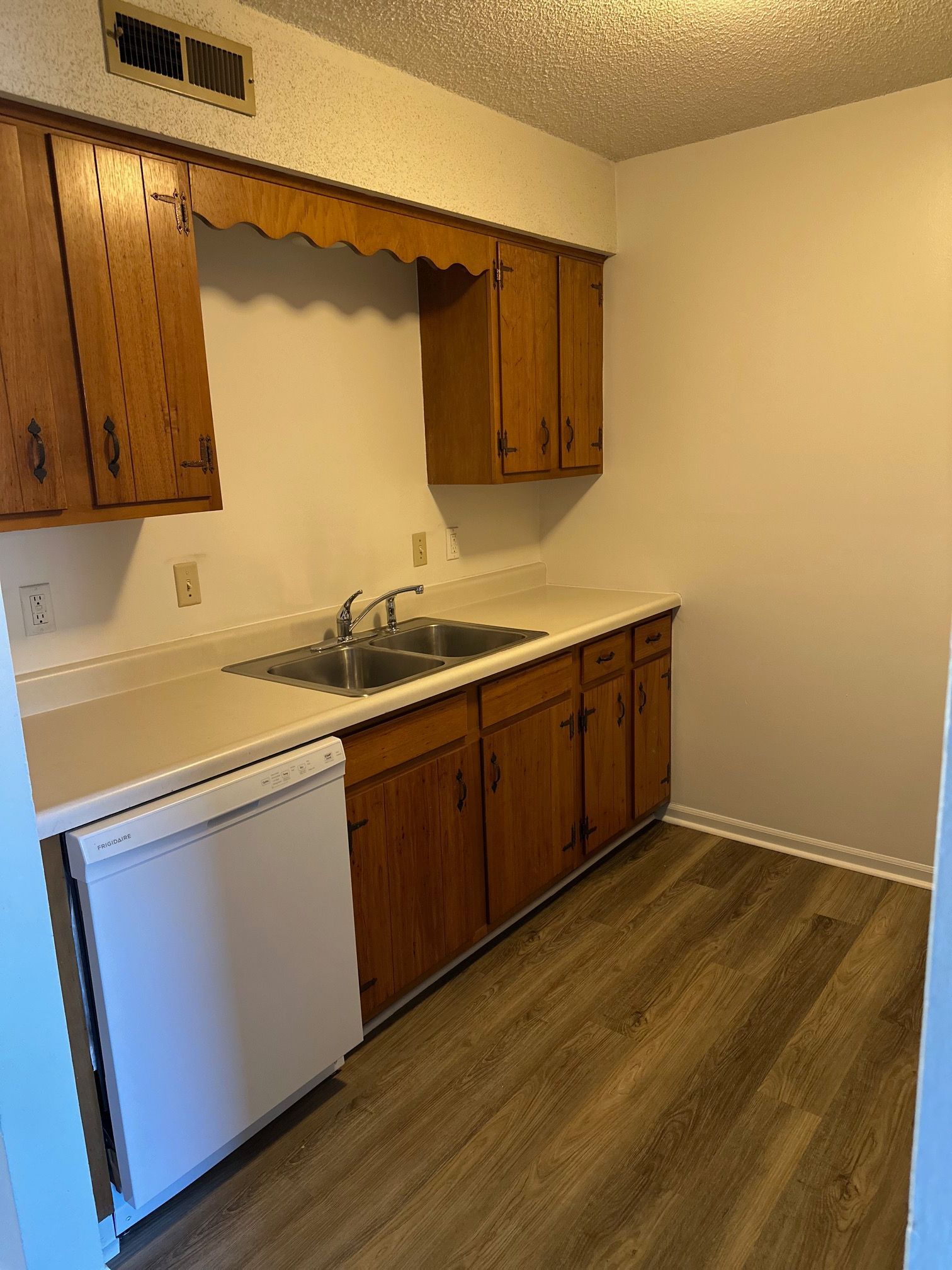 Small kitchen with wood cabinets, white countertops, sink, dishwasher, and wood-look flooring.