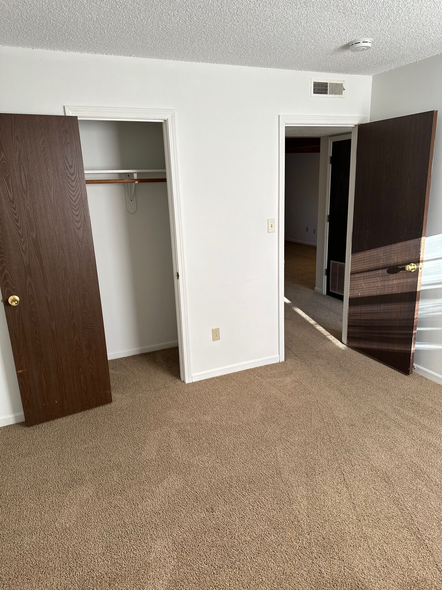Empty beige-carpeted bedroom with open closet and open doorway on white walls