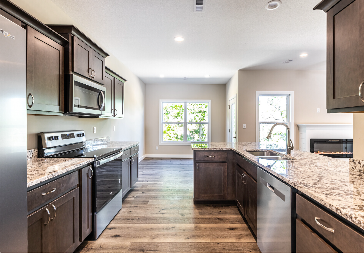 Modern kitchen with dark cabinets, granite counters, stainless appliances, and a large window at the back.