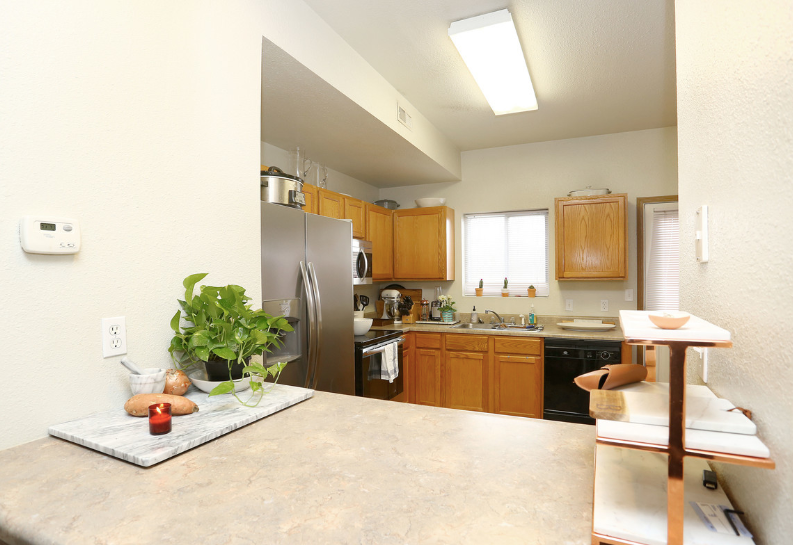Bright kitchen with wooden cabinets, stainless fridge, beige counters, and a small plant on the counter.