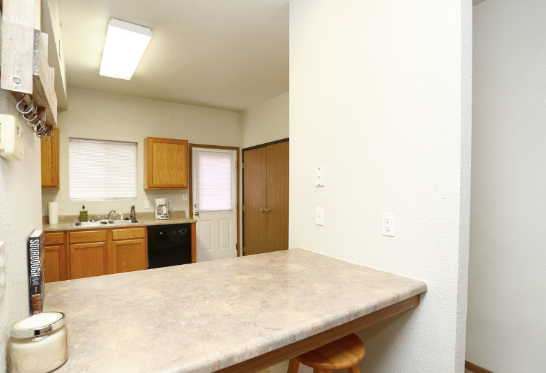 Empty kitchen with beige counters, wood cabinets, sink, stove, and a door at the back.