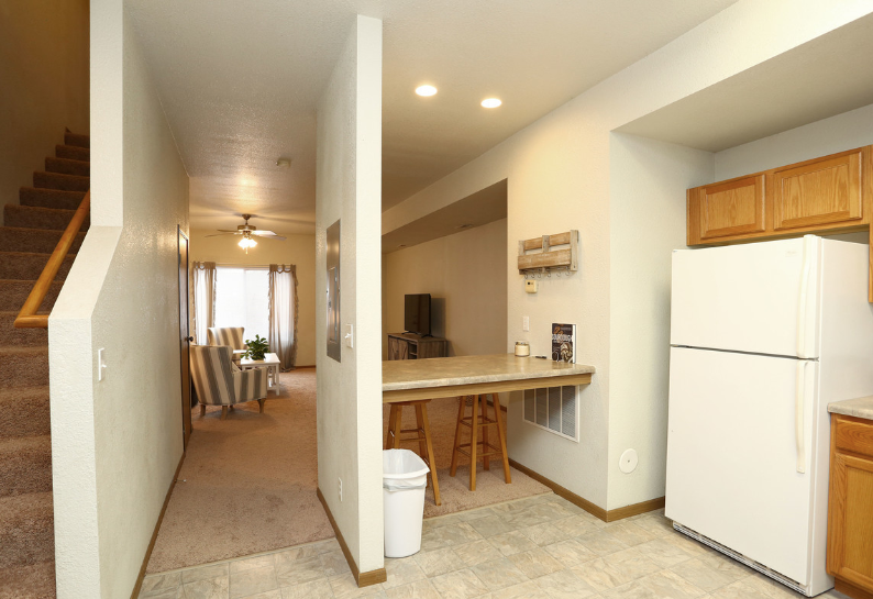 Interior of a small kitchen and hallway with a white fridge, breakfast bar, and staircase leading upstairs.