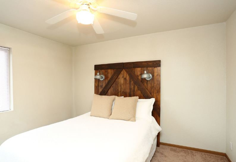 Bright bedroom with a bed, wooden headboard, white walls, and ceiling fan.