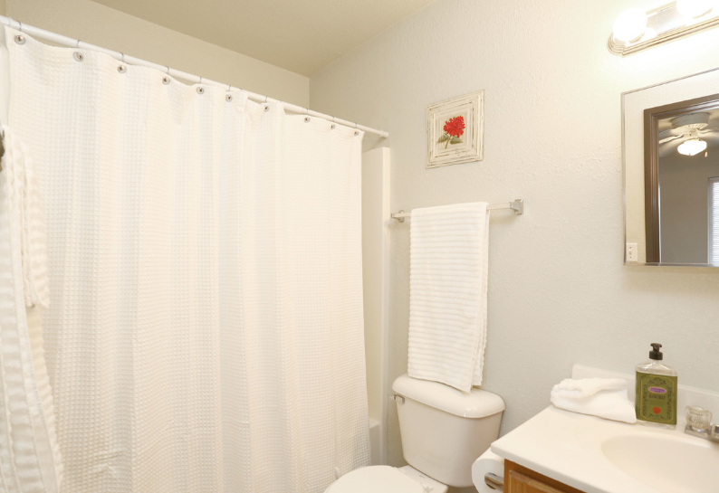 Small bathroom with a shower curtain, toilet, sink, and wall mirror under soft lighting