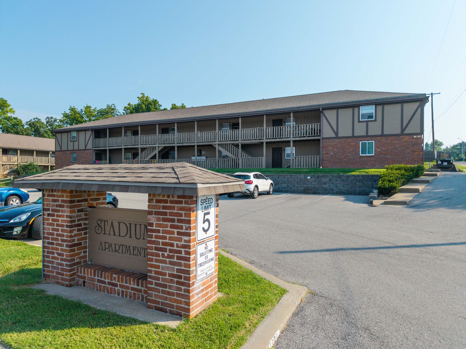 Brick stadium entrance sign with landscaped shrubs and a building in the background