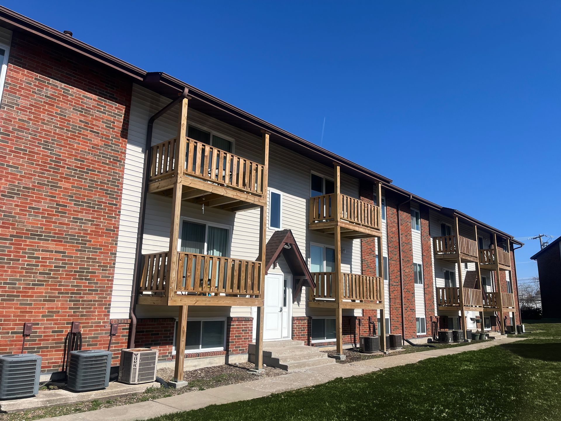 Apartment building with red brick walls and wooden balconies under a clear blue sky