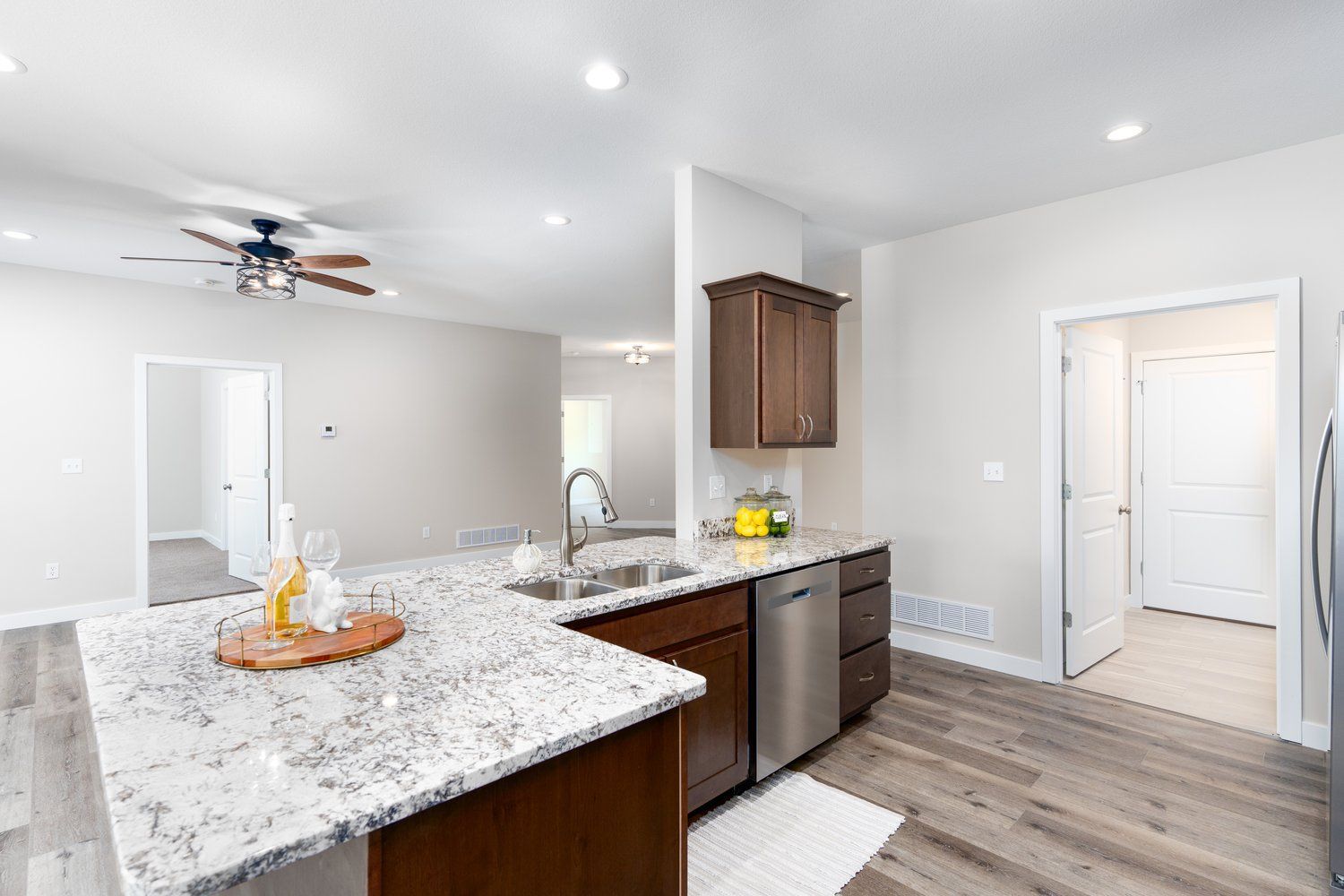 Bright modern kitchen with granite island, dark wood cabinets, recessed lights, and wood-look flooring.