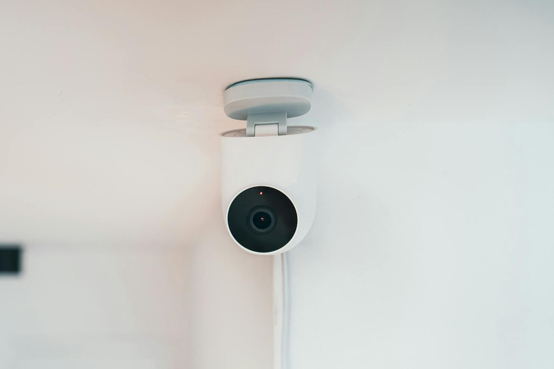 A white security camera is mounted on a white wall.