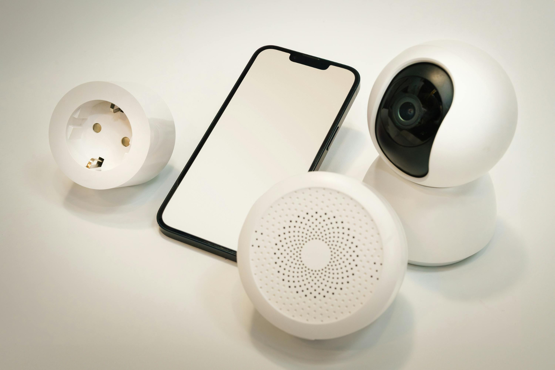 A smart phone , a camera , a socket and a speaker are on a table.