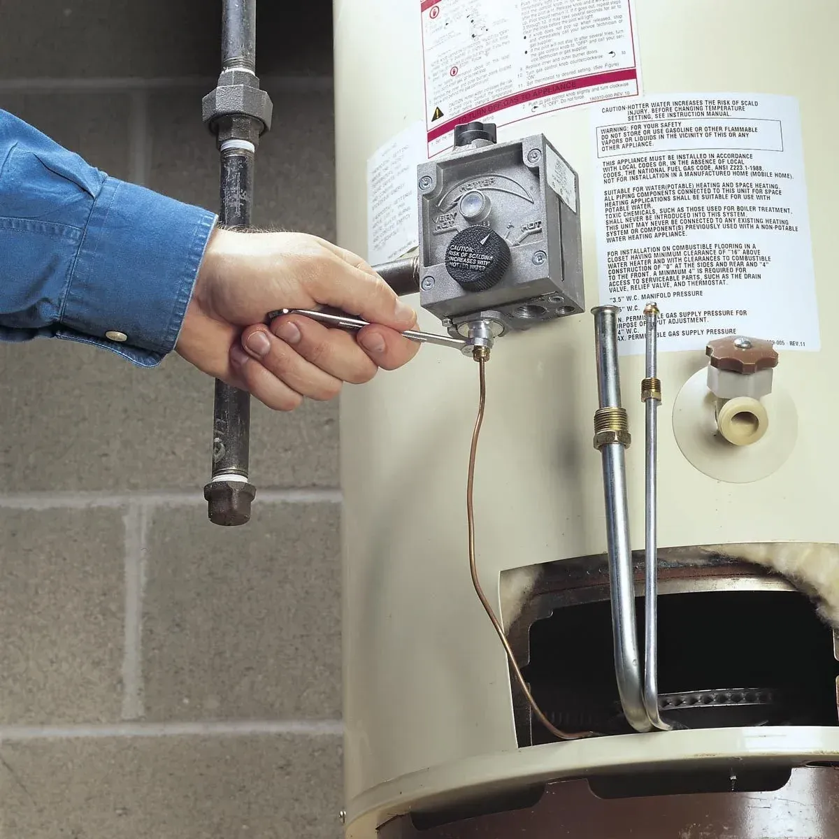 A person is fixing a water heater with a wrench