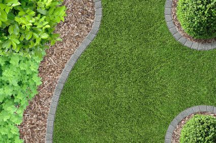 Curved stone-bordered garden path beside green grass and shrubs with mulch around them
