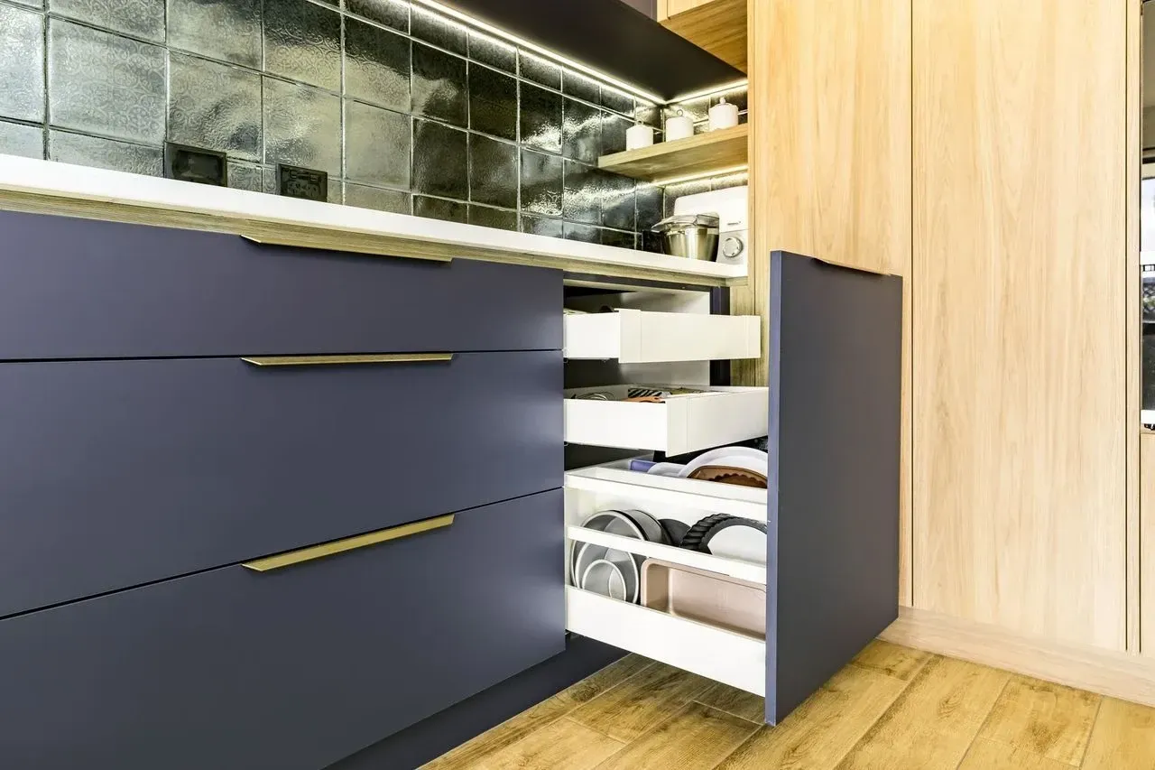 A kitchen with blue cabinets and wooden floors and drawers open.