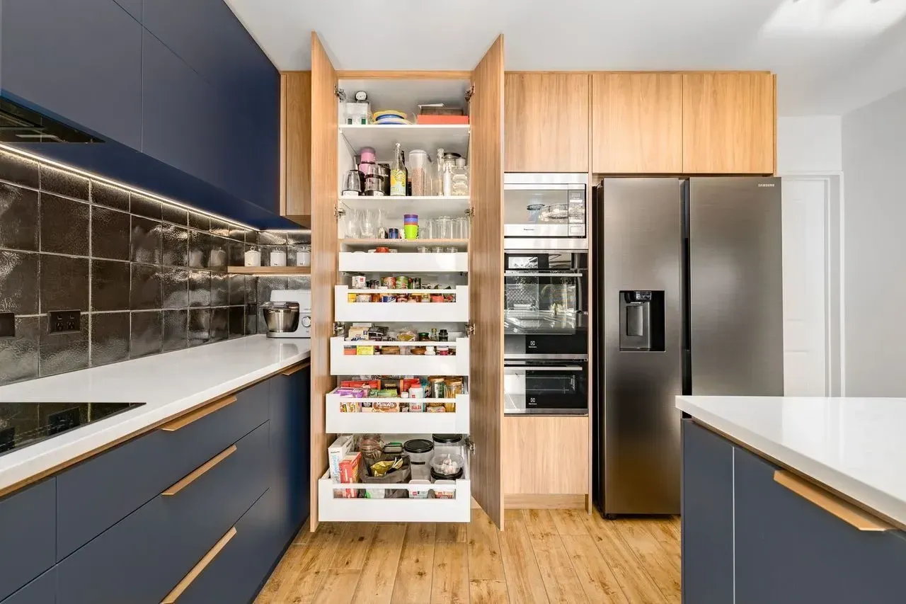 A kitchen with blue cabinets , a stainless steel refrigerator , and a pantry with drawers.