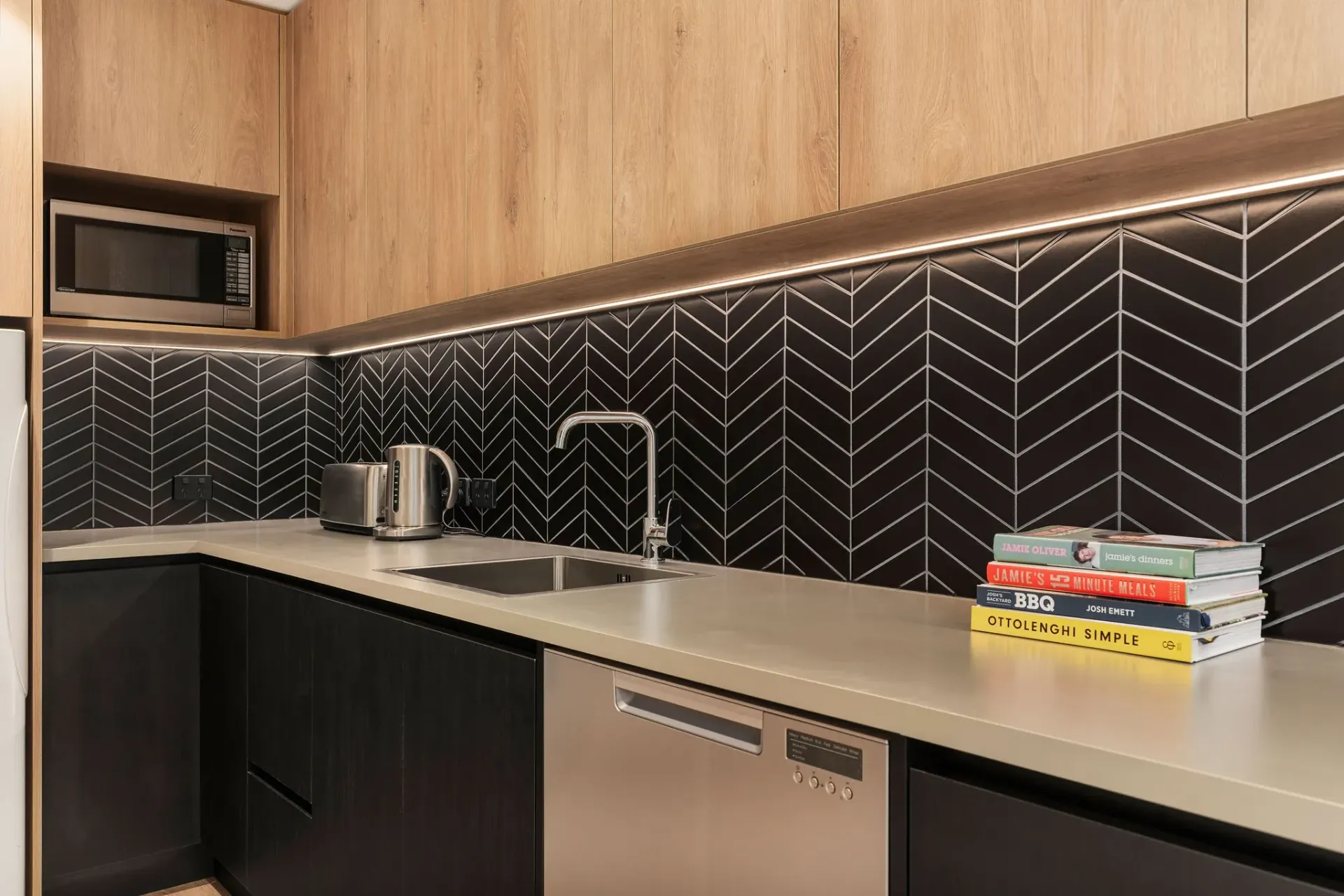 A kitchen with a sink , dishwasher , microwave and books on the counter.