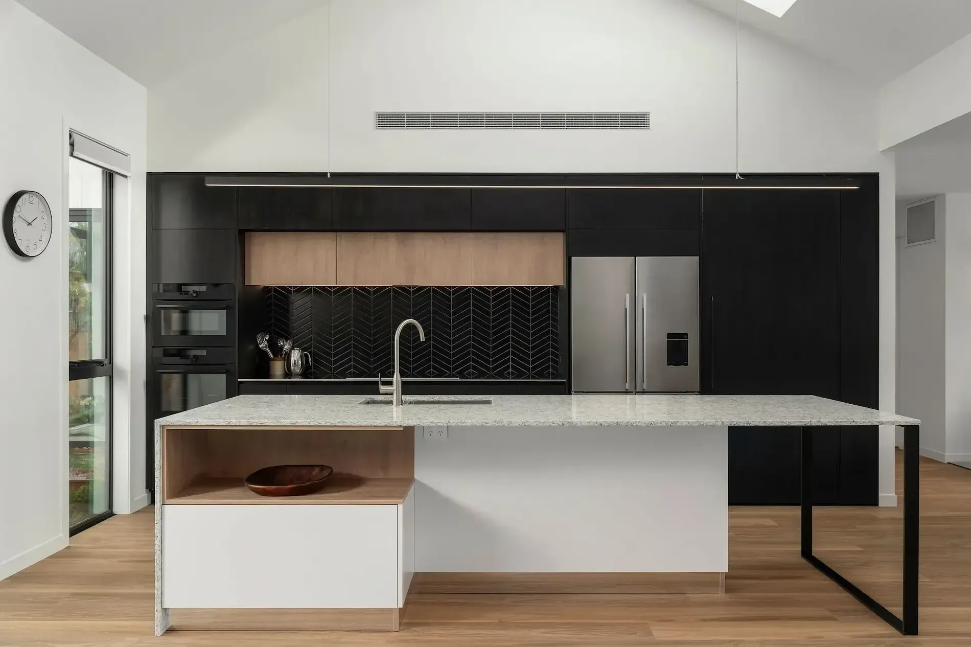 A kitchen with black cabinets , white counter tops , and a stainless steel refrigerator.