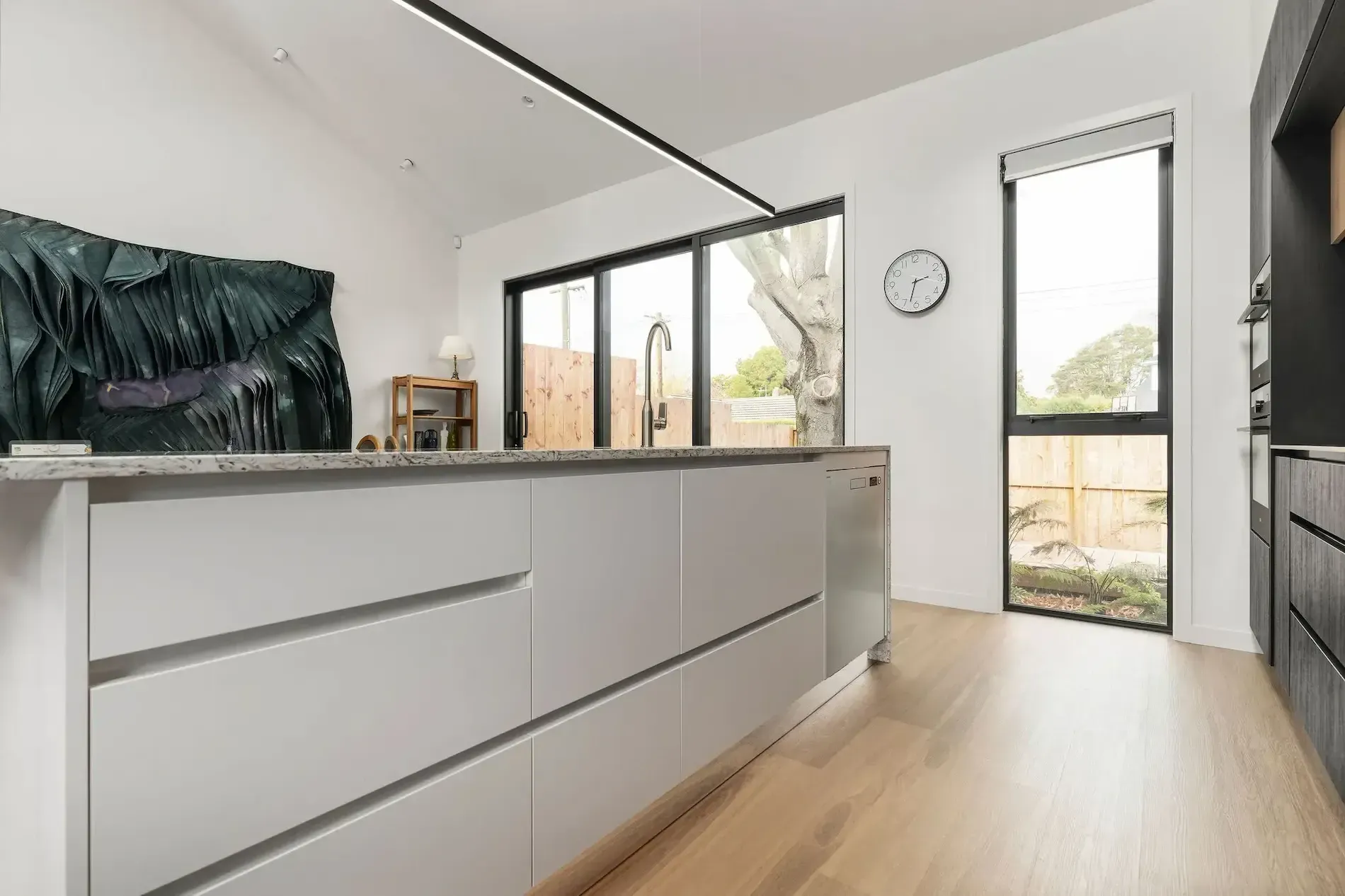 A kitchen with white cabinets , a large island , a sink , and a clock on the wall.